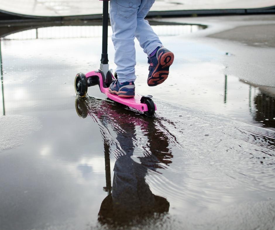 child on scooter going through a puddle