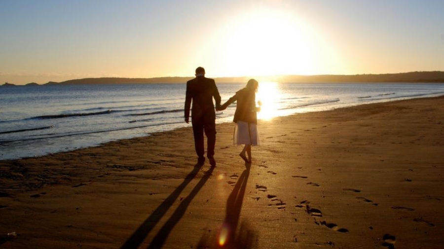 couple walking holding hands on beach at sunset