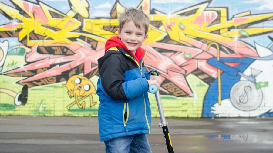 child on scooter in front of colourful wall